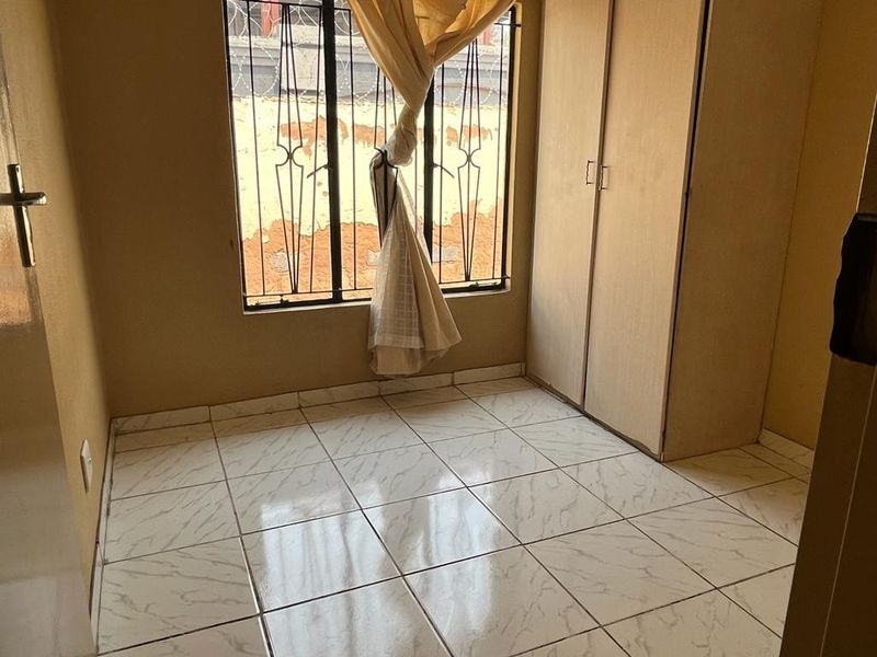 A compact bedroom featuring tiled flooring, a built-in wardrobe, and security bars on the window.