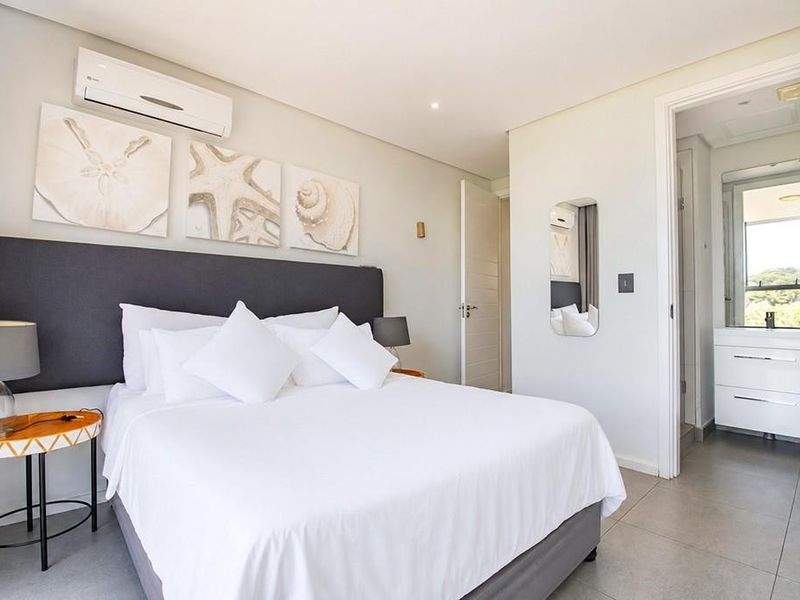 A well-maintained bedroom featuring tiled flooring, recessed lighting, a wall-mounted air conditioning unit, and direct access to an en-suite bathroom.