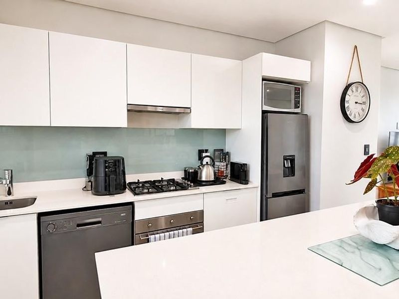 Modern kitchen featuring sleek white cabinetry, stone countertops, a central island, and high-quality stainless steel appliances including a gas hob and integrated dishwasher.