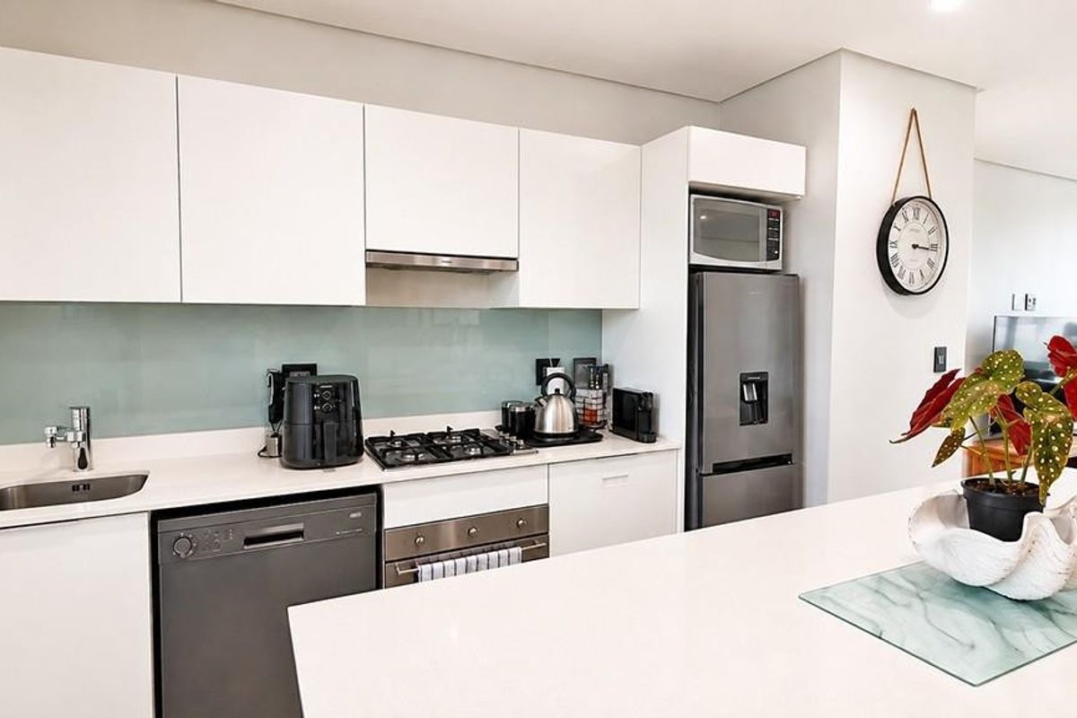 Modern kitchen featuring sleek white cabinetry, stone countertops, a central island, and high-quality stainless steel appliances including a gas hob and integrated dishwasher.