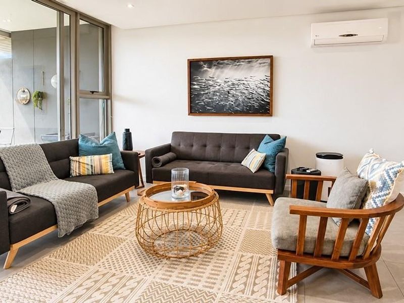 A bright and modern living room featuring large sliding glass doors, tiled flooring, and a wall-mounted split-system air conditioner.