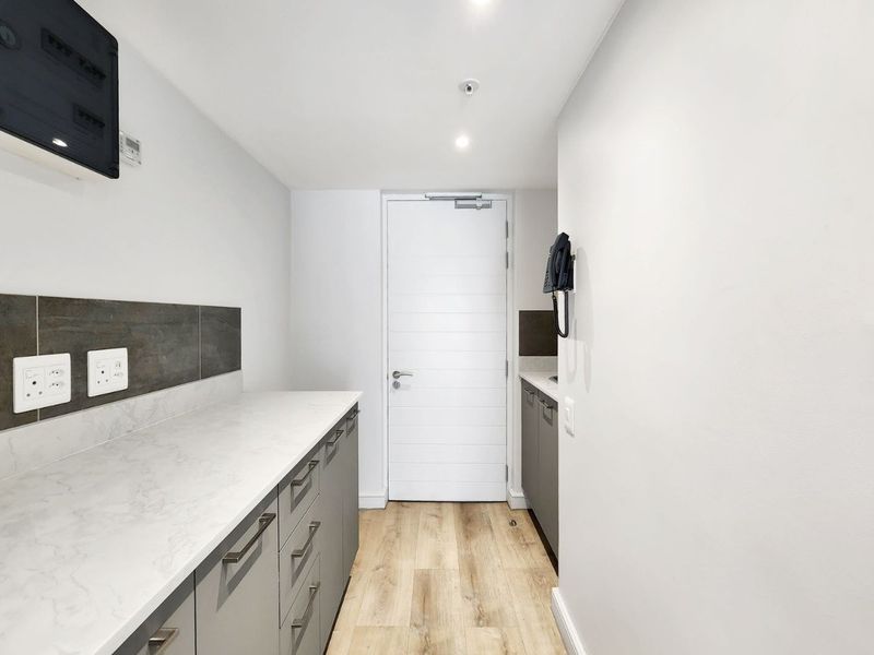 A clean, modern scullery or utility area featuring sleek grey cabinetry, stone countertops, tiled backsplash, and durable laminate flooring.