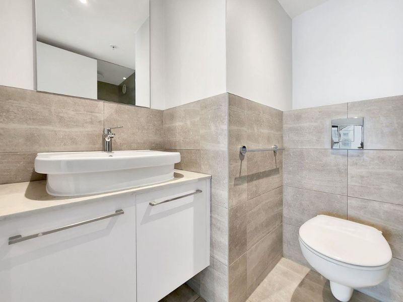 Modern bathroom featuring a wall-mounted vanity with a vessel sink, wall-hung toilet with concealed cistern, and neutral ceramic tiling.