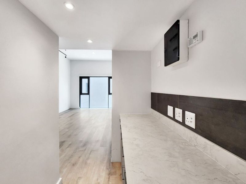 A clean, modern scullery or utility area featuring a stone countertop, tiled splashback, and integrated electrical services, leading into an open-plan living space.
