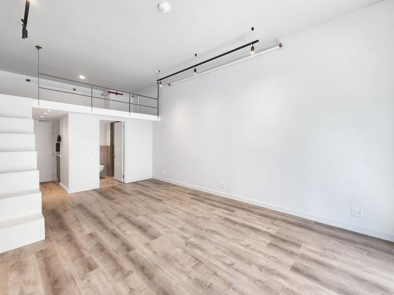 Spacious open-plan living area featuring a mezzanine level, modern laminate flooring, track lighting, and a clean, minimalist aesthetic.