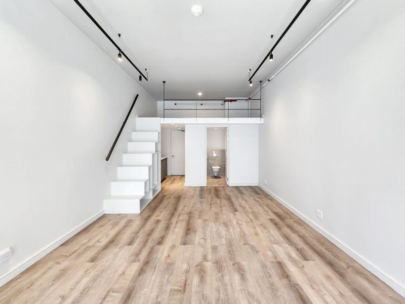 Modern open-plan apartment featuring a mezzanine level, laminate flooring, track lighting, and a compact bathroom, offering a versatile and contemporary living space.