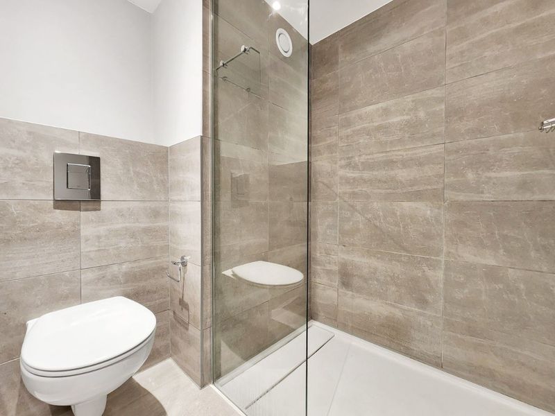 Modern bathroom featuring a walk-in shower with glass screen, integrated shower seat, and a wall-mounted toilet with a sleek flush plate.