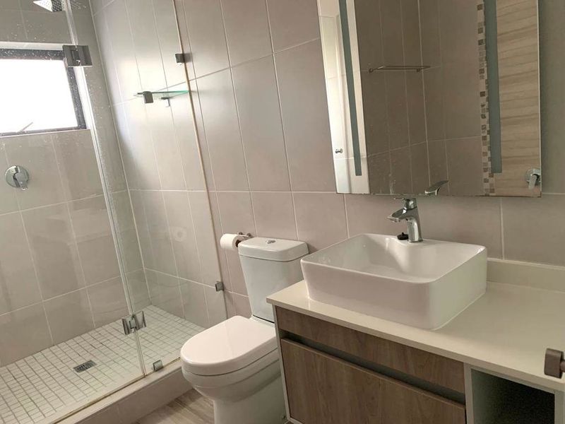 Modern bathroom featuring a glass-enclosed shower, a contemporary vessel sink on a vanity cabinet, and neutral wall tiling.