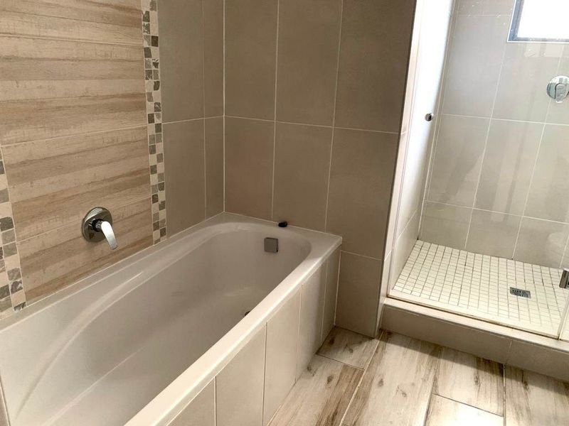Modern bathroom featuring a built-in bathtub, separate shower enclosure, and neutral tiled finishes throughout.