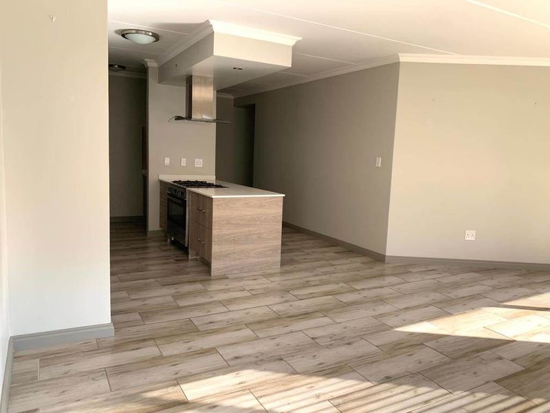 Open-plan living area featuring a modern kitchen island with built-in oven, gas hob, and stainless steel extractor fan, complemented by wood-look tile flooring.