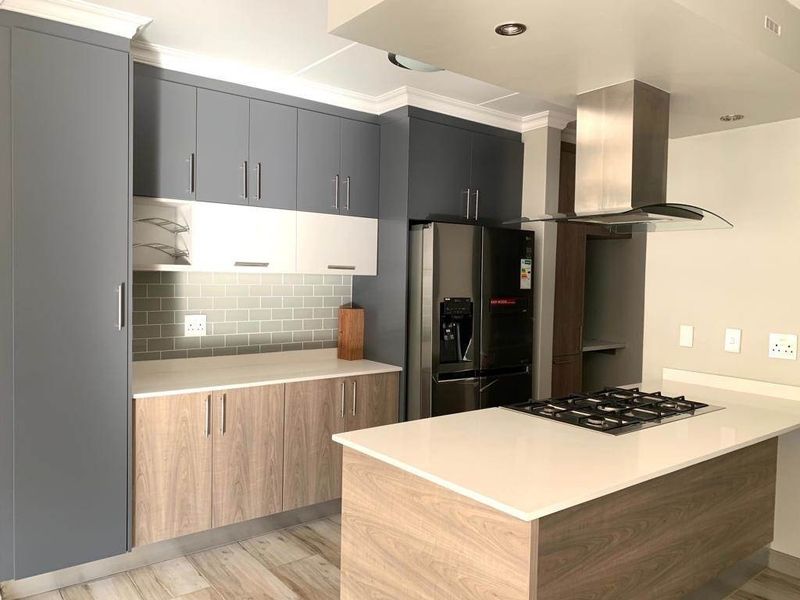 Modern kitchen featuring two-tone cabinetry, quartz countertops, a central island with a gas hob, and a sleek stainless steel extractor fan.