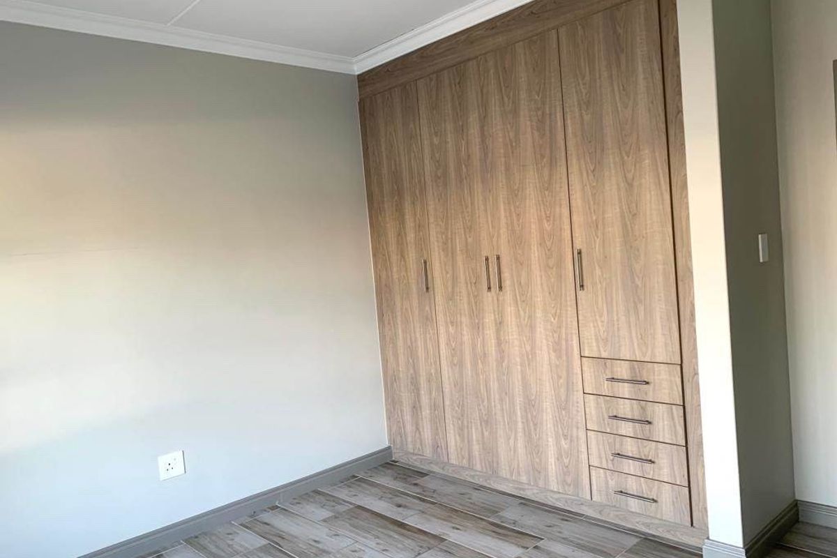 A clean, modern bedroom featuring wood-look tile flooring and extensive built-in wooden cabinetry with integrated drawers.