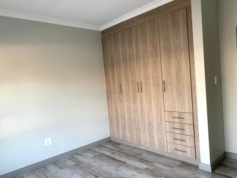 A clean, modern bedroom featuring wood-look tile flooring and extensive built-in wooden cabinetry with integrated drawers.