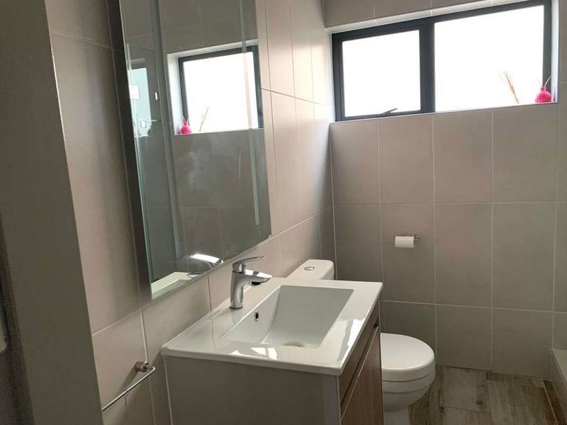 Modern bathroom featuring a vanity cabinet with a ceramic basin, chrome mixer tap, wall-mounted mirror, and neutral wall and floor tiling.
