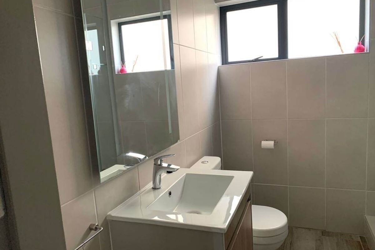 Modern bathroom featuring a vanity cabinet with a ceramic basin, chrome mixer tap, wall-mounted mirror, and neutral wall and floor tiling.