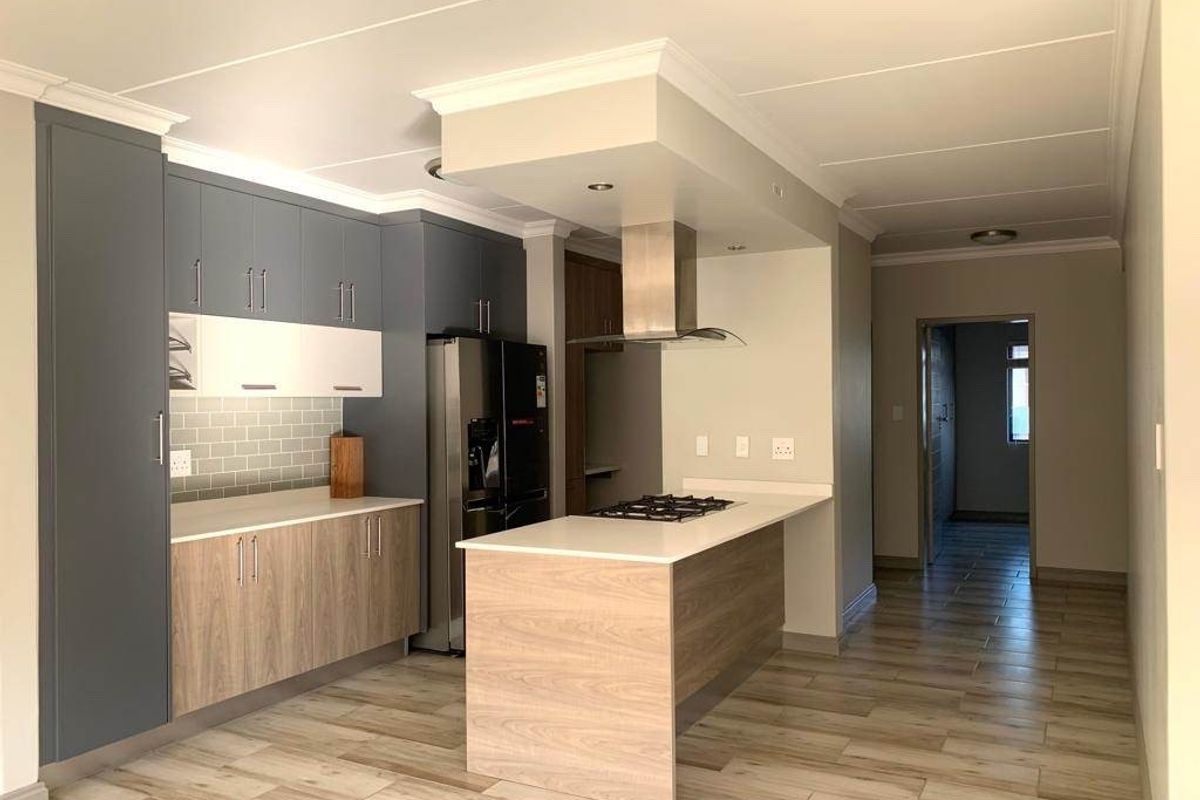 Modern kitchen featuring two-tone cabinetry, stone countertops, a central island with a gas hob, extractor fan, and stylish subway tile backsplash.
