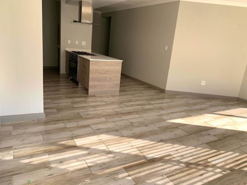 An open-plan living and kitchen area featuring modern wood-look tile flooring, a central kitchen island with a built-in oven, hob, and stainless steel extractor.