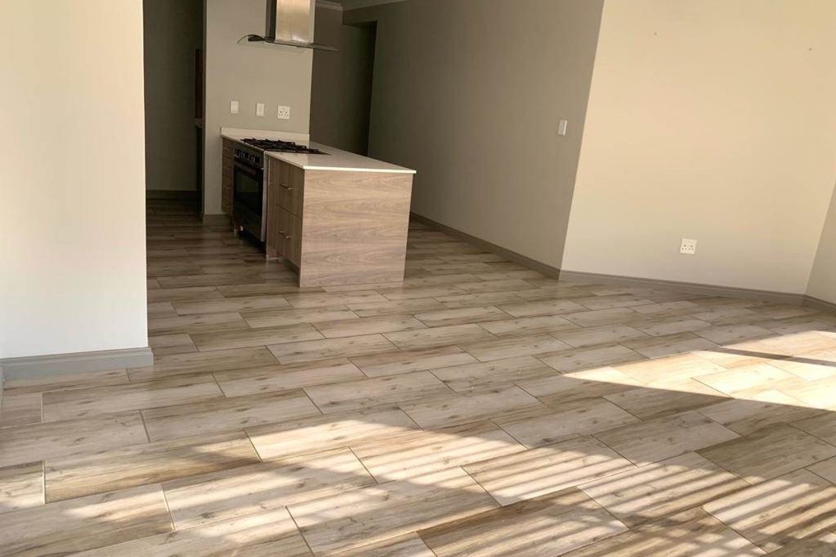 An open-plan living and kitchen area featuring modern wood-look tile flooring, a central kitchen island with a built-in oven, hob, and stainless steel extractor.