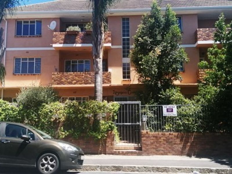 Front elevation of a multi-story apartment building featuring brick facade, private balconies, and a secure gated entrance with perimeter brick walling.