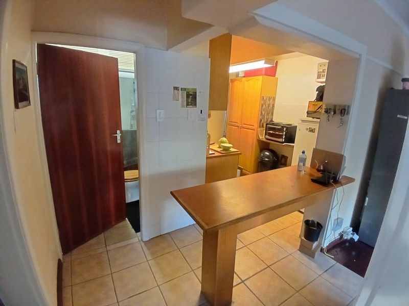 A compact kitchen area featuring tiled flooring, built-in cabinetry, and a breakfast bar, with an adjacent doorway leading to a bathroom.