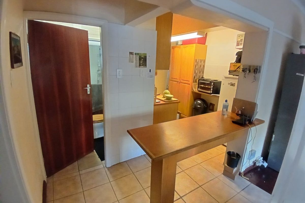 A compact kitchen area featuring tiled flooring, built-in cabinetry, and a breakfast bar, with an adjacent doorway leading to a bathroom.