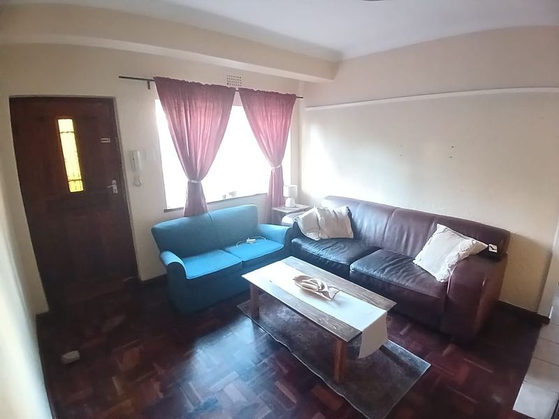 A living room featuring dark parquet flooring, a timber entrance door, and an intercom system, providing a functional space with potential for cosmetic updates.