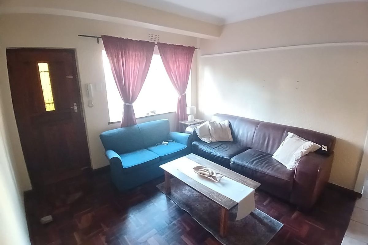 A living room featuring dark parquet flooring, a timber entrance door, and an intercom system, providing a functional space with potential for cosmetic updates.