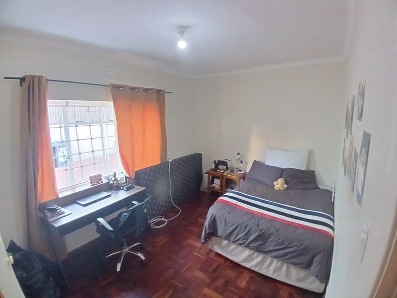 A bedroom featuring parquet flooring and a window fitted with security bars.