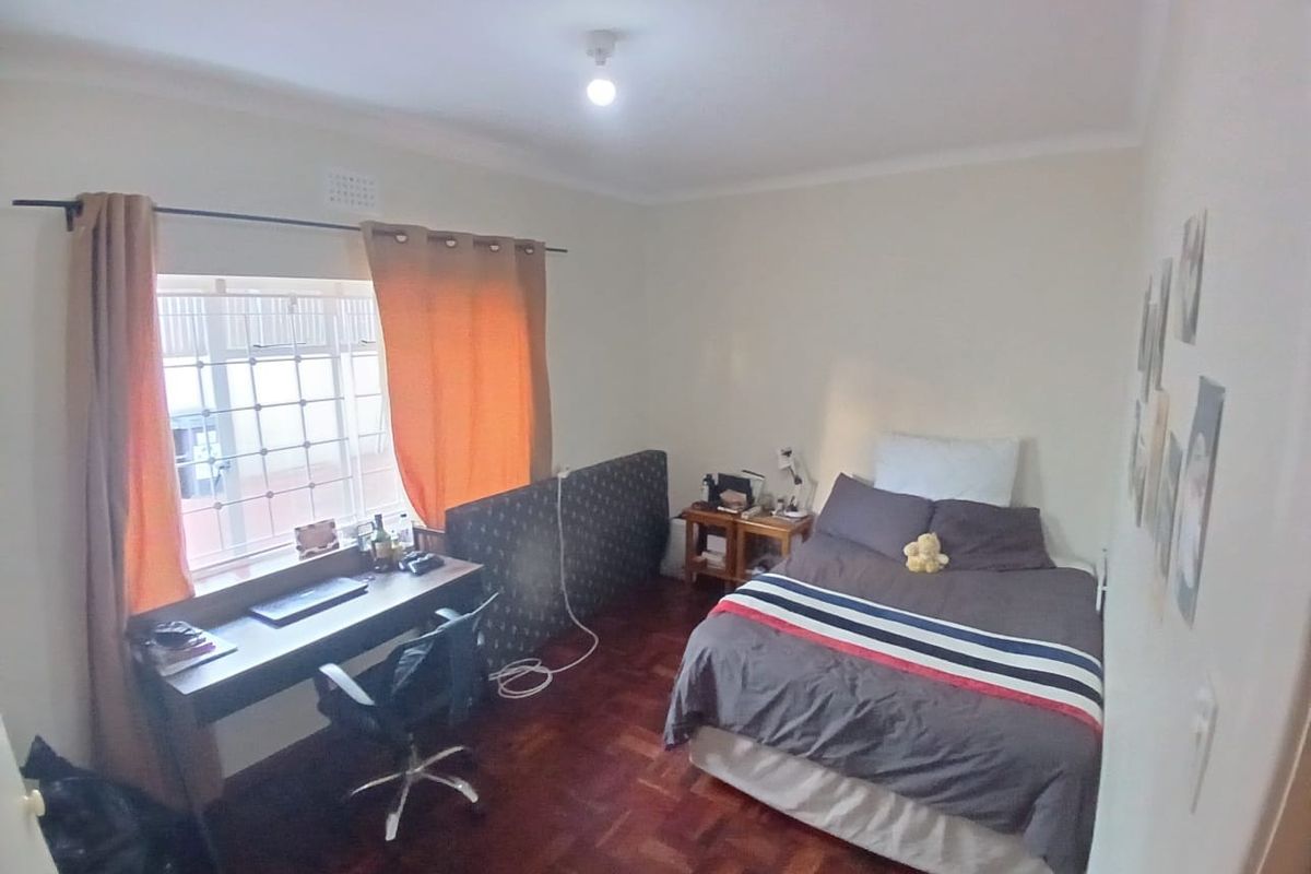 A bedroom featuring parquet flooring and a window fitted with security bars.