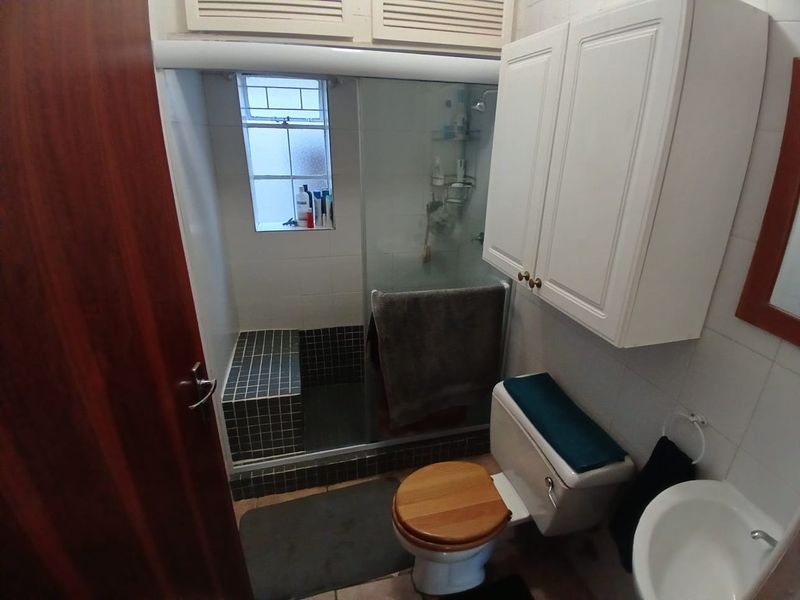 Compact bathroom featuring a tiled shower enclosure with a built-in bench, pedestal basin, toilet, and wall-mounted storage cabinetry.
