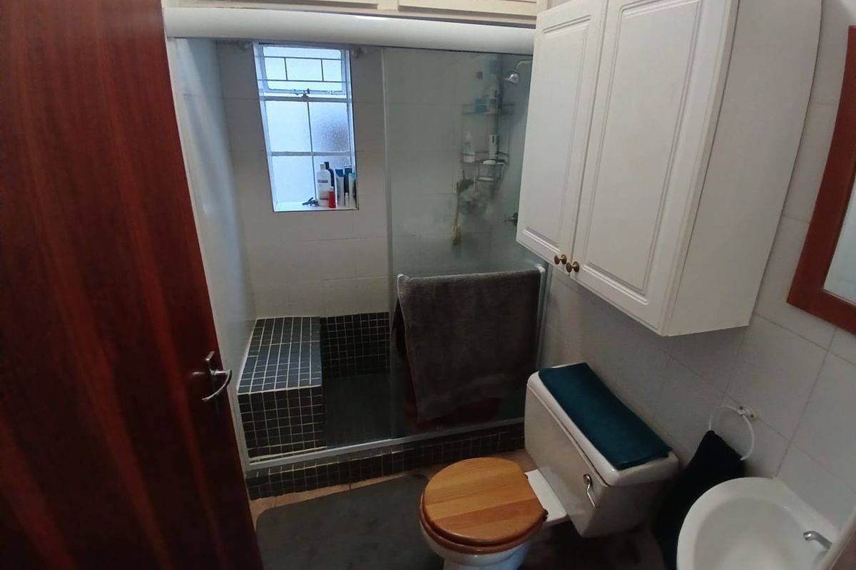 Compact bathroom featuring a tiled shower enclosure with a built-in bench, pedestal basin, toilet, and wall-mounted storage cabinetry.