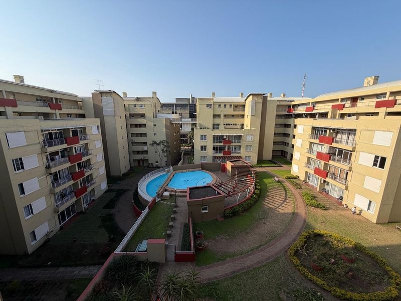 Aerial view of an apartment complex courtyard featuring a central swimming pool, landscaped gardens, and paved walkways between residential buildings.