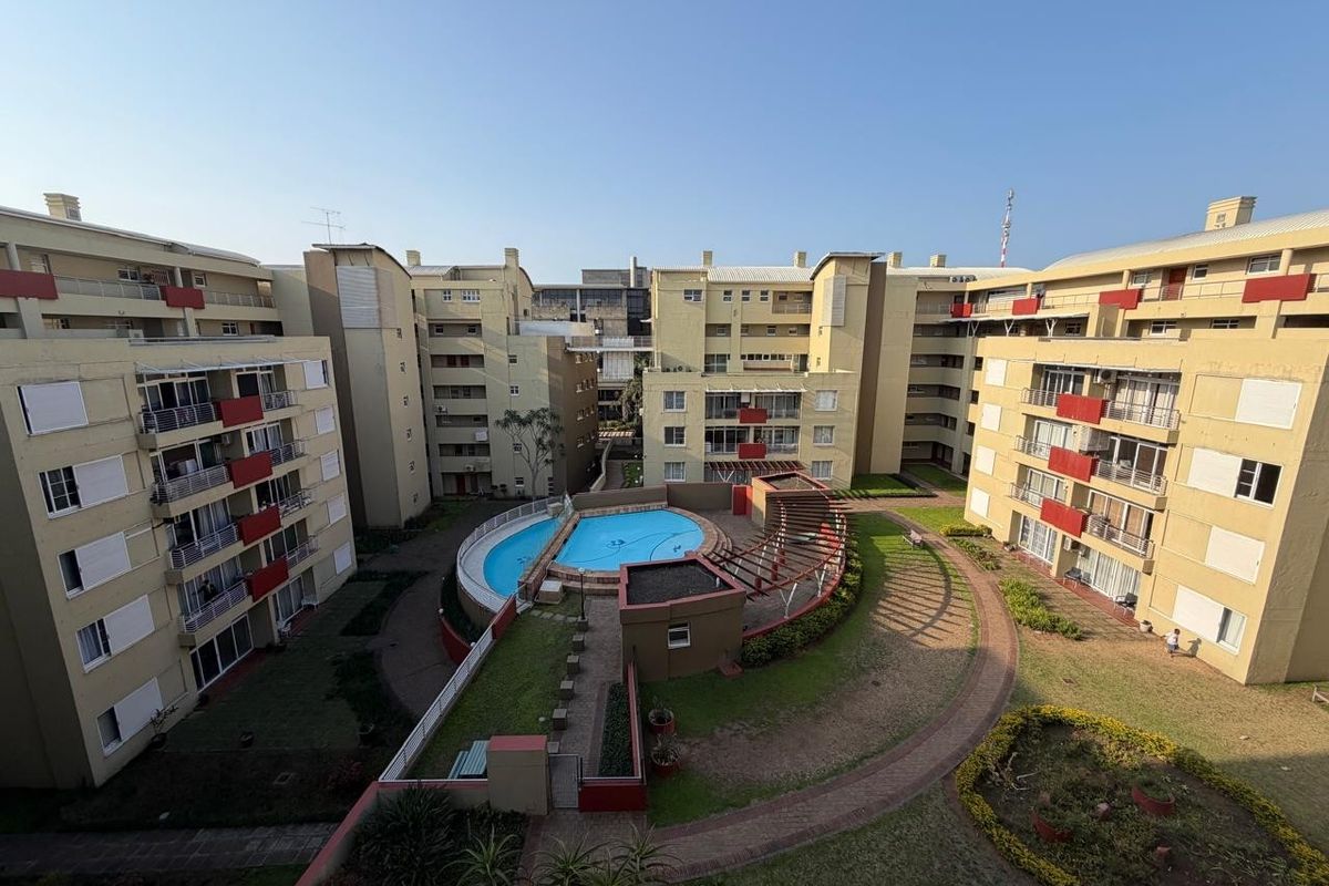 Aerial view of an apartment complex courtyard featuring a central swimming pool, landscaped gardens, and paved walkways between residential buildings.