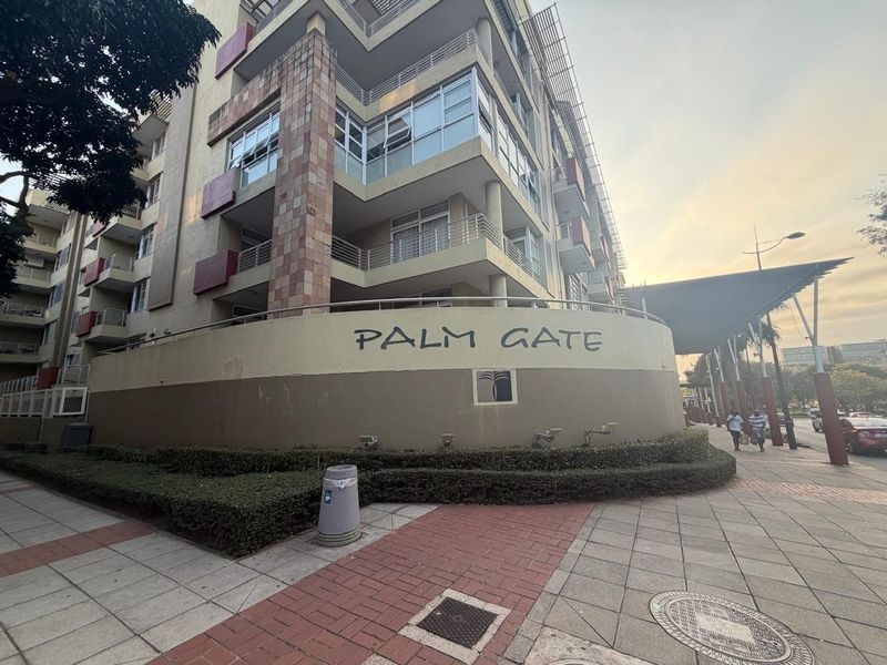 Exterior view of the Palm Gate apartment complex featuring multi-level balconies and paved pedestrian access.