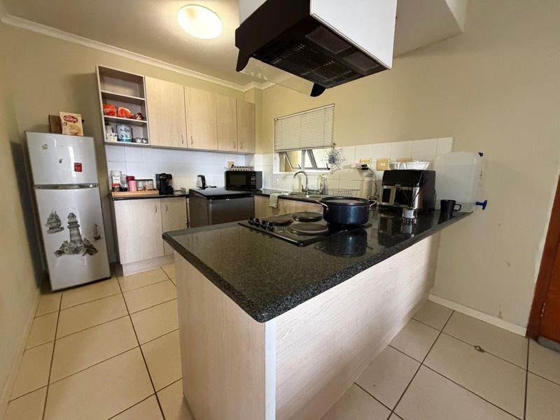 Functional kitchen featuring laminate cabinetry, granite countertops, an electric hob with extractor fan, and tiled flooring.