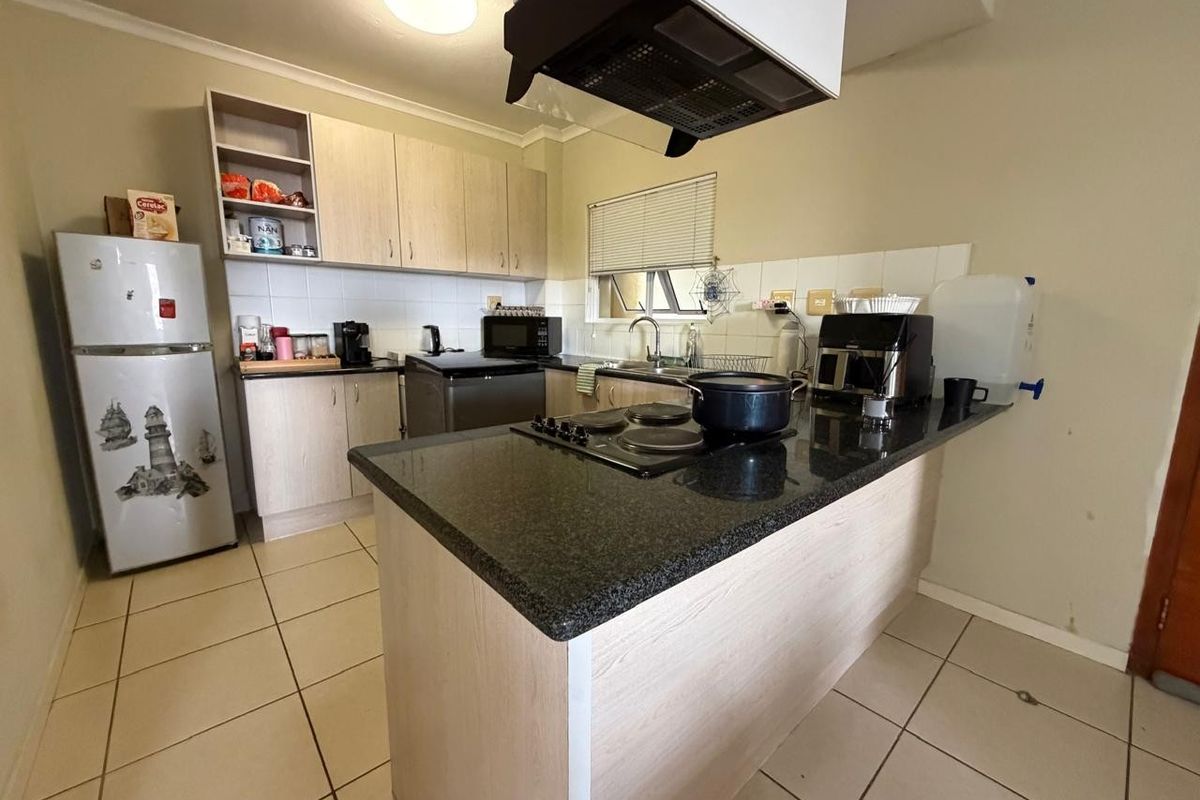 Functional kitchen featuring laminate cabinetry, granite countertops, an electric hob with extractor fan, and tiled flooring.