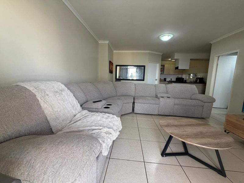 Open plan living area featuring tiled flooring and a connected kitchen space with built-in cabinetry and an extractor fan.