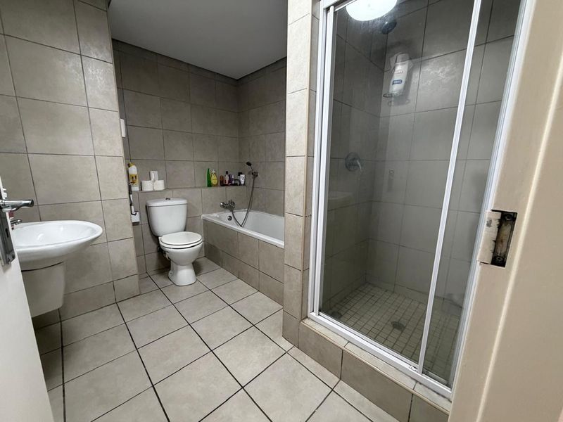 A functional bathroom featuring tiled walls and floors, a separate shower enclosure, a built-in bathtub, and a wall-mounted basin.