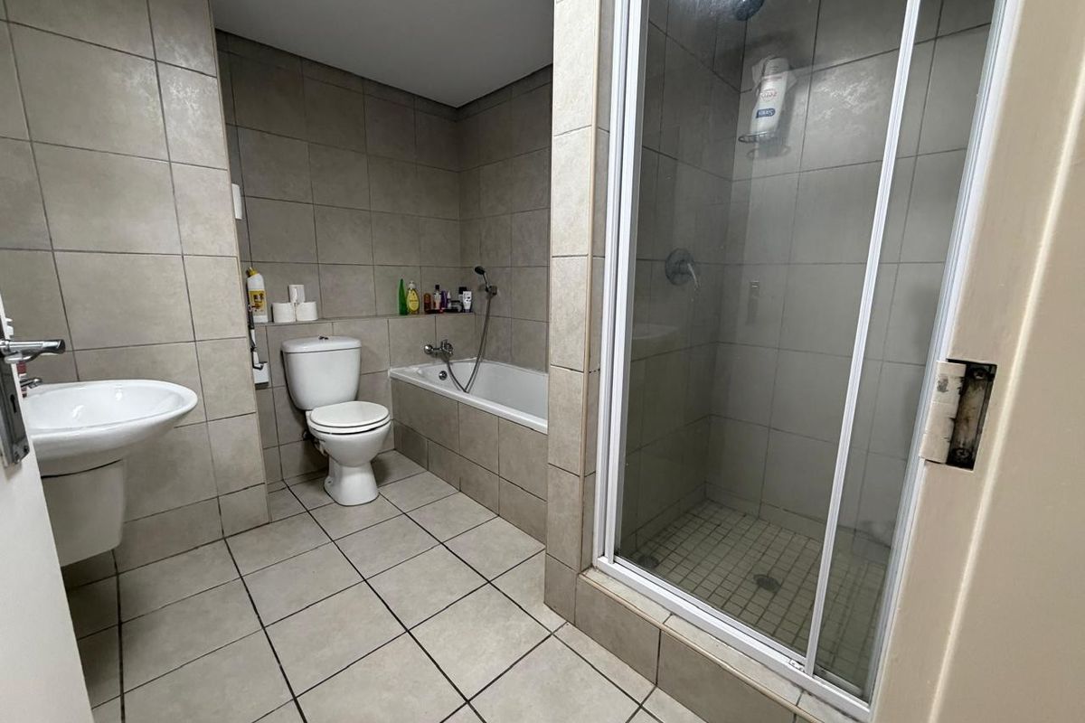 A functional bathroom featuring tiled walls and floors, a separate shower enclosure, a built-in bathtub, and a wall-mounted basin.