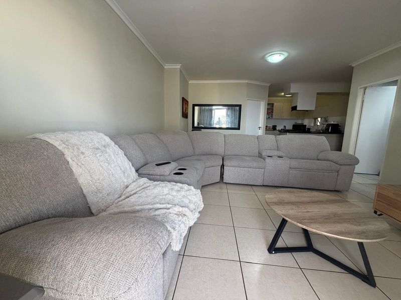 Open plan living area featuring tiled flooring and a connected kitchen space with built-in cabinetry and an extractor fan.