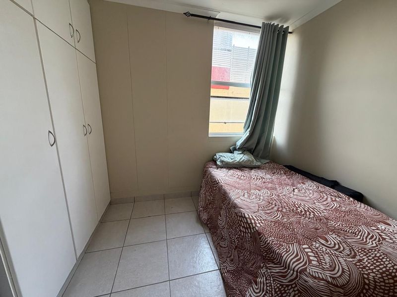 A compact bedroom featuring tiled flooring and built-in cupboards, providing functional storage space.