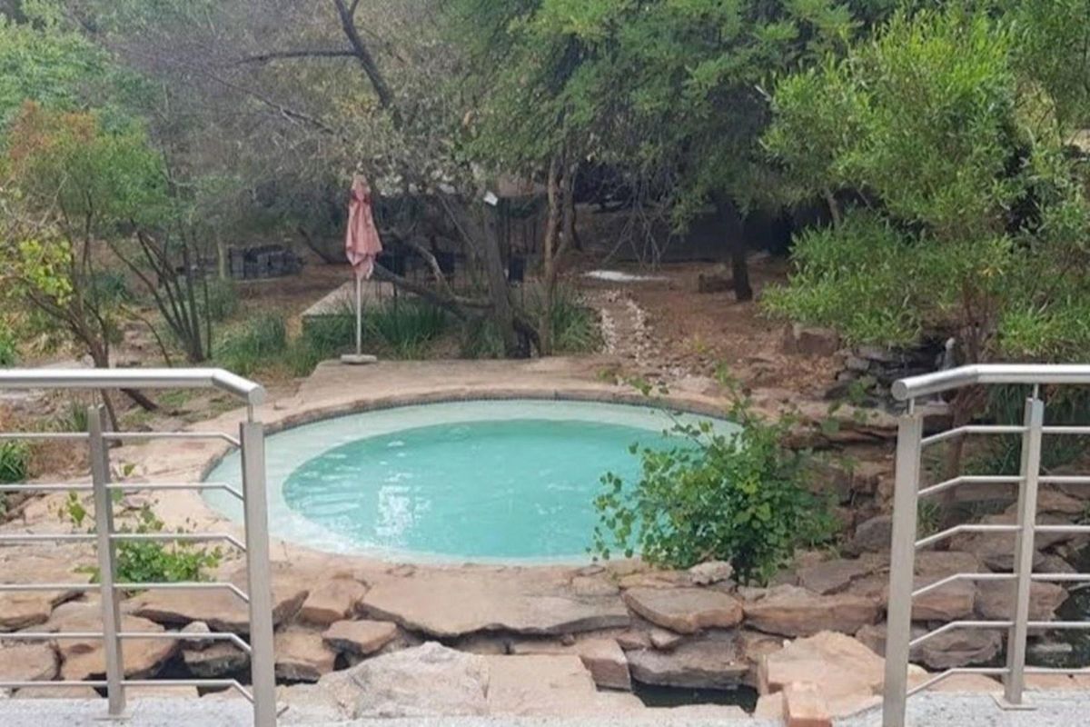 A circular swimming pool set within a natural stone surround, featuring stainless steel railings and a landscaped garden setting.