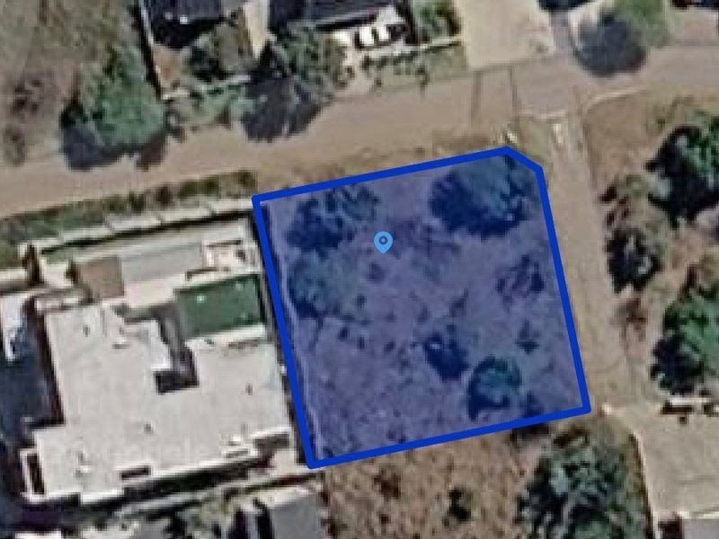 An aerial view of a vacant residential plot, highlighting the property boundaries and surrounding neighborhood context.