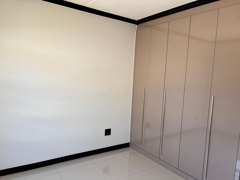 A clean, modern bedroom featuring high-gloss built-in wardrobes, neutral tiled flooring, and contrasting dark skirting boards.