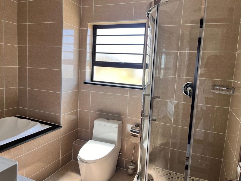 A modern, well-maintained bathroom featuring a built-in bathtub, a separate glass-enclosed shower, and neutral floor-to-ceiling tiling.