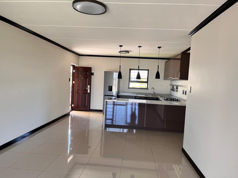 Modern open-plan living area featuring a sleek kitchen with glossy cabinetry, stone countertops, built-in hob, and polished tiled flooring throughout.