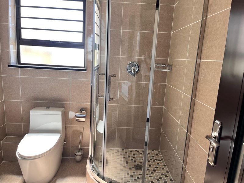 A clean, modern bathroom featuring a glass-enclosed shower, neutral wall tiling, and a contemporary toilet.