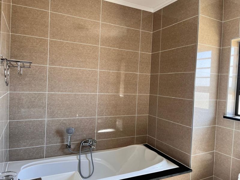 A clean, modern bathroom featuring a built-in bathtub with chrome fixtures and neutral-toned wall tiling.