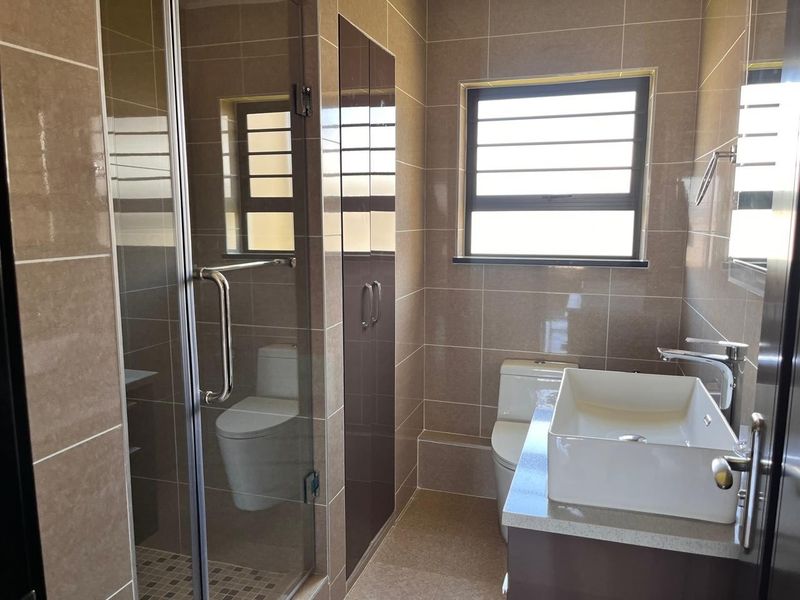 Modern bathroom featuring a glass-enclosed shower, vessel sink on a vanity cabinet, toilet, and neutral wall tiling.