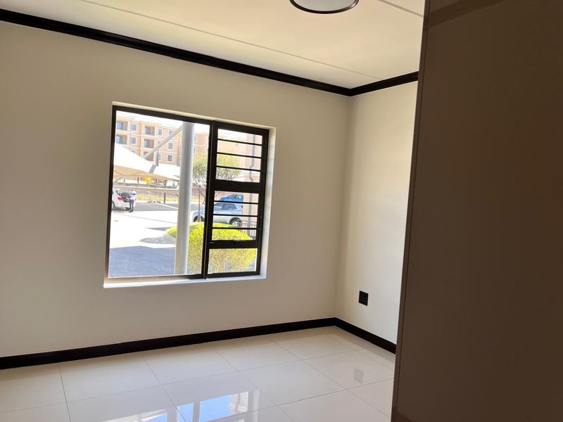 A bright, empty bedroom featuring neutral tiled flooring, dark skirting boards, and an aluminium window with integrated security bars.